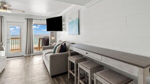 Un salon moderne avec un canapé, une table basse et un téléviseur fixé au mur. Il y a un balcon avec vue sur l’océan.
