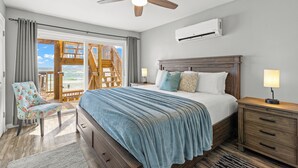 Une chambre à coucher comprenant un lit, une table de chevet, une chaise, un ventilateur de plafond et une vue sur l’extérieur.