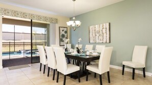 A dining area with a table set for six, surrounded by white chairs, a chandelier, and a painting on the wall. - 8BR ChampionsGate | Cinema, Arcade & Private Pool (Davenport)