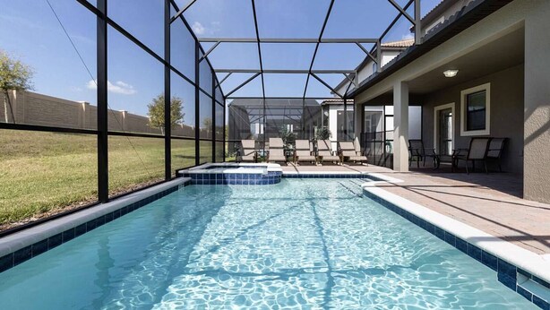 A swimming pool with a glass enclosure, lounge chairs, and a patio area. - 8BR ChampionsGate | Cinema, Arcade & Private Pool (Davenport)