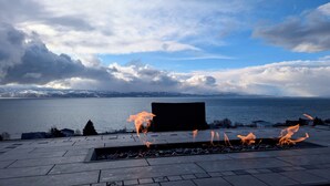 Une terrasse dotée d’un foyer extérieur, offrant une vue sur un plan d’eau et des montagnes.