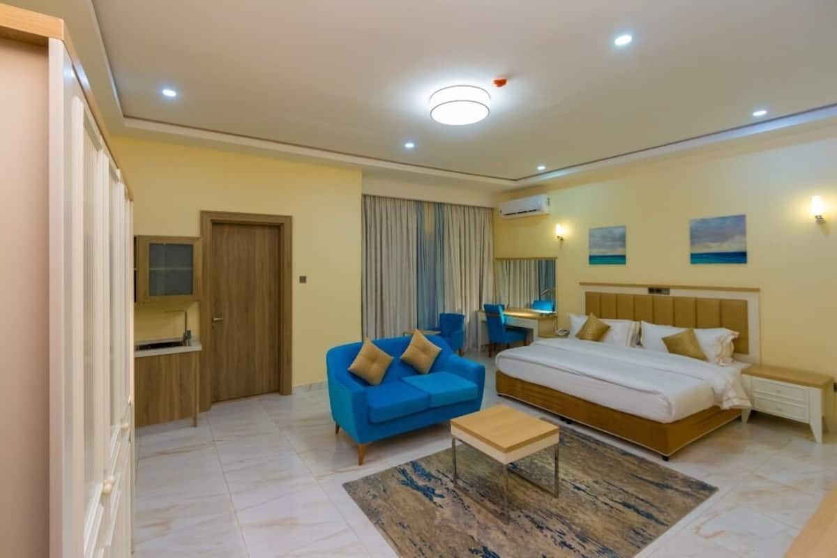 Una habitación de hotel con una cama, un sofá azul, una mesita, un escritorio y un aire acondicionado.