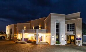A modern hotel with a brick facade, large windows, and a well-lit entrance. - HERA (Abuja)