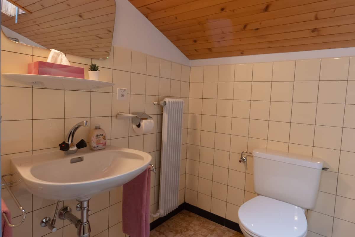 A bathroom with a wooden ceiling, a white sink, a toilet, and a tiled floor.