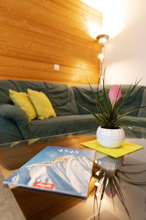 Een woonkamer met een glazen bijzettafeltje, een potplant en een boek.
