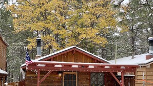 A wooden cabin with a porch, a flag, and a snow-covered landscape.