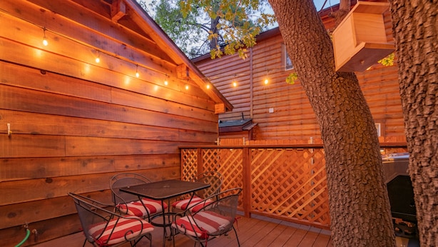An outdoor patio with wooden walls, string lights, a metal table with chairs, and a wooden fence.