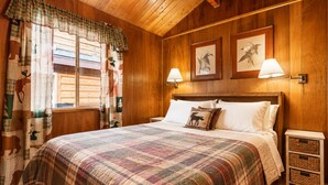 A wooden-paneled room with a bed, two wall-mounted lamps, and a window with curtains.