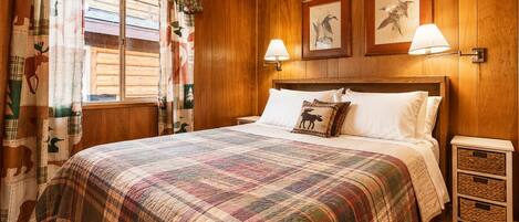 A wooden-paneled room with a bed, two wall-mounted lamps, and a window with curtains.