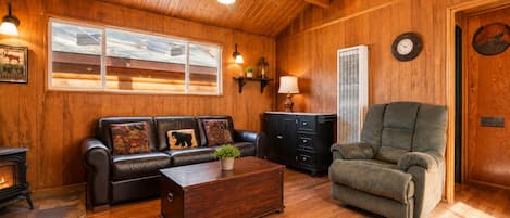 A cozy living room with a fireplace, leather sofa, armchair, and a wooden coffee table.