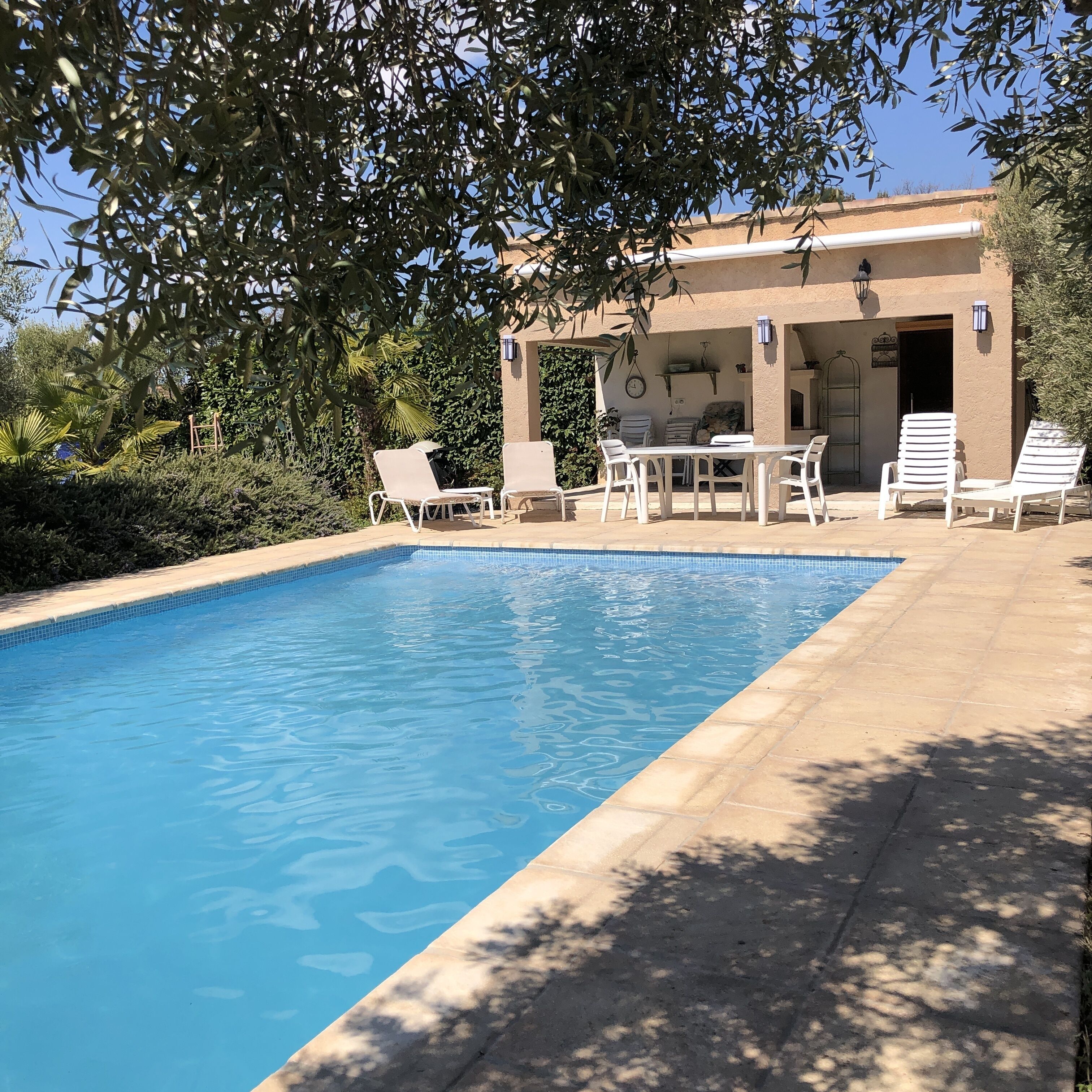 A clear blue pool with white lounge chairs and a covered patio area.