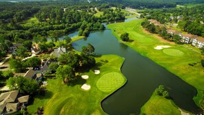 An aerial view of a golf course with a pond, surrounded by residential buildings and lush greenery. - 2nd floor 2 BR, 2 bath, Sunset Beach 5 mins from Ocean @ Sea Trail Golf Resort  (Sunset Beach)