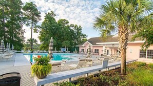 A pool area with lounge chairs and umbrellas, surrounded by trees and a building with a pink facade. - 2nd floor 2 BR, 2 bath, Sunset Beach 5 mins from Ocean @ Sea Trail Golf Resort  (Sunset Beach)