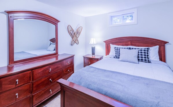 Een slaapkamer met een houten dressoir, een bed met hoofdeinde, een nachtkastje met een lamp en een spiegel aan de muur.
