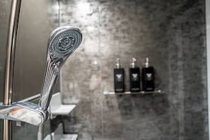 Une salle de bain dotée d’une douche moderne, d’un mur en marbre et d’une étagère contenant des articles de toilette.