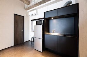Compact kitchen with microwave, refrigerator, and air conditioning unit.