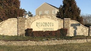 A stone wall with the text "REHOBOTH CROSSING" in the center, surrounded by a landscaped area with grass and shrubs. - Spacious 4 Bed, 4,5 bath. Pet friendly. Come enjoy Rehoboth! (Rehoboth Beach)