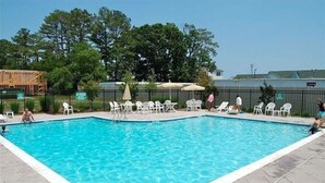 A rectangular swimming pool with clear blue water, surrounded by white lounge chairs and umbrellas, set against a backdrop of trees and a fence. - Spacious 4 Bed, 4,5 bath. Pet friendly. Come enjoy Rehoboth! (Rehoboth Beach)