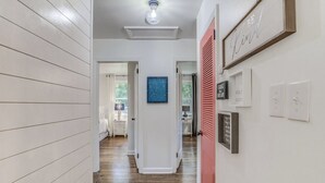 Un couloir doté d’un plancher en bois, de murs blancs et d’un luminaire au plafond. On y trouve des portes menant à d’autres pièces, un tableau bleu accroché au mur et un panneau affichant un texte motivant.