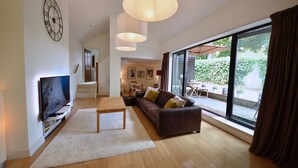 A modern living room with a flat-screen TV, a sofa, a coffee table, and a large window with curtains. - Spacious Open Plan House in Central Windsor. Dog Friendly + Off Street Parking! (Windsor)