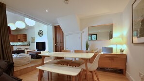 A modern living room with a dining area, wooden furniture, a flat-screen TV, and a large mirror. - Spacious Open Plan House in Central Windsor. Dog Friendly + Off Street Parking! (Windsor)