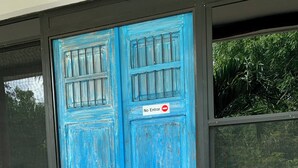 Een blauwe deur met een 'No Entrar' bord, bloempotten en een metalen karretje ervoor.