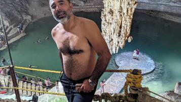 Un hombre está de pie sobre un saliente rocoso, contemplando una piscina natural con estalactitas.