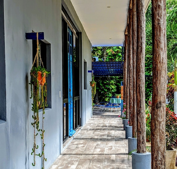 A covered corridor with a tiled floor, a blue chair, and potted plants.