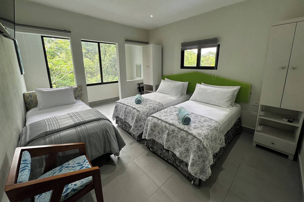 Une chambre d’hôtel avec deux lits, une chaise, une armoire et une fenêtre donnant sur un paysage verdoyant.
