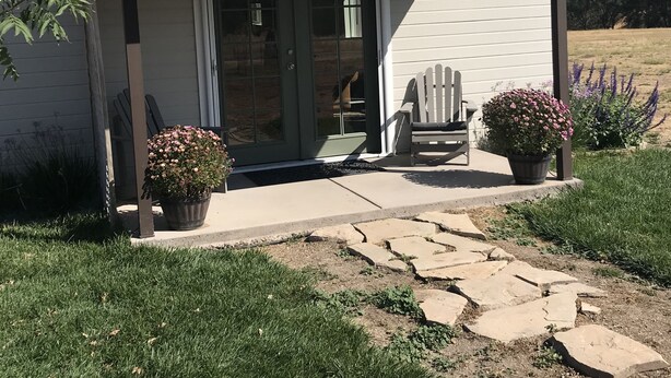 Une petite maison de plain-pied avec un porche couvert, une porte et deux plantes en pot.