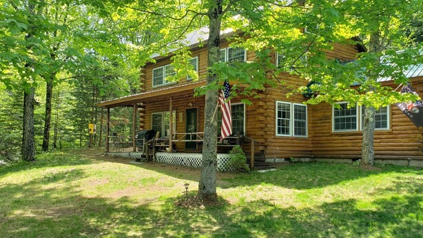 Une cabane en rondins avec un porche, un drapeau américain et une terrasse en bois.