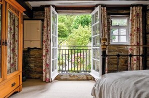 Relax in a serene bedroom with a large window overlooking a lush garden, featuring a comfortable bed and a wooden wardrobe.
