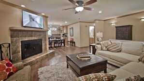 A spacious living room with a fireplace, a ceiling fan, and a television mounted on the wall. - Rural Beauty with Urban Convenience (Hot Springs)