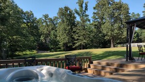 A hot tub with a wooden deck and chairs, surrounded by a grassy yard and trees. - Rural Beauty with Urban Convenience (Hot Springs)