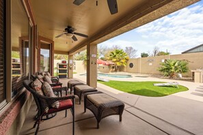 A covered patio with wicker furniture, a ceiling fan, and a view of a swimming pool and lawn.