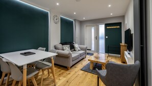 Un salon moderne avec un canapé, une table à manger et des chaises. Il y a une horloge au mur et un téléviseur fixé au mur.