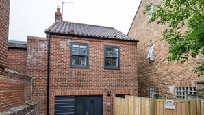 Un bâtiment en briques avec une porte de garage noire, une clôture en bois et une enseigne indiquant « 85A ».