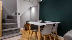 Un intérieur moderne avec un escalier, une table blanche avec des chaises et un mur d’accent vert foncé.