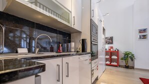 A modern kitchen with a black countertop, stainless steel appliances, and a red shoe rack.