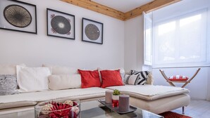 A modern living room with a white sofa, red and patterned cushions, a glass coffee table with decorative items, and framed wall art.