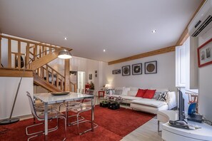A spacious living area with a staircase, a dining table with chairs, a sofa, and a red carpet.