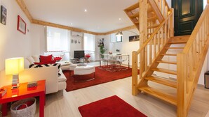 A modern living room with a wooden staircase, a dining area, and a TV in the background.