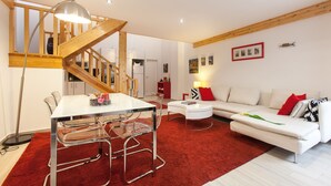 A modern living room with a dining area, a staircase, and a kitchen in the background.