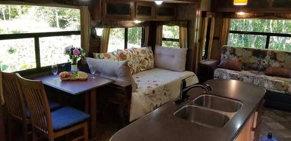 A cozy RV interior with a dining area, a bed with floral bedding, and a kitchenette.