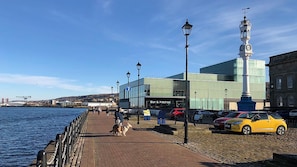 A waterfront promenade with a bar and kitchen restaurant, a dog walking, and parked cars. - Central 1-bed Apt, Sleeps 4, 5 Mins to Station (Greenock)