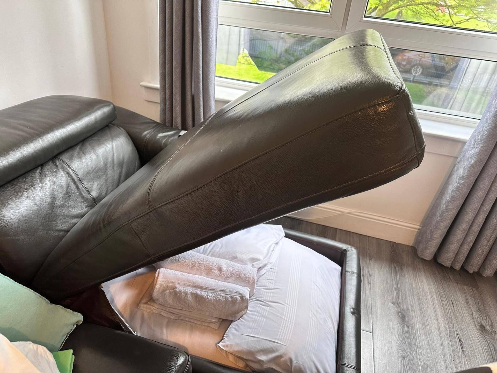 A leather recliner chair with a footrest and a white pillow.