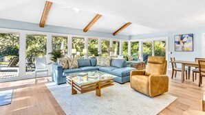 A spacious living room with a sectional sofa, a glass coffee table, and a dining area with wooden furniture. - Exquisite Home w/ Private Pool & Dock Hilton Head (Hilton Head Island)