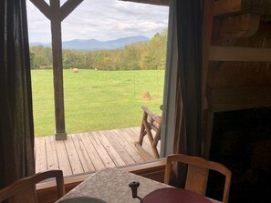 A wooden deck with a table and chairs, overlooking a grassy field with hay bales and distant mountains. - Hand hewn log cabin with beautiful views of the Blue Ridge Mountains  (Roseland)