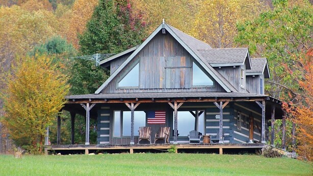 Une cabane rustique dotée d’un porche, d’un drapeau américain et surplombant une forêt.
