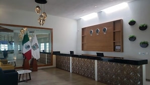 A modern reception area with a wooden reception desk, a large mirror, and a wall-mounted clock. - Hotel Plaza Matamoros (Matamoros)